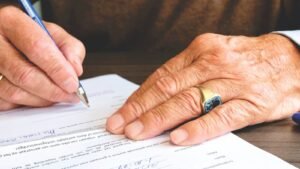 Elderly person signing a legal document by hand, representing wills and estate planning in Pakistan